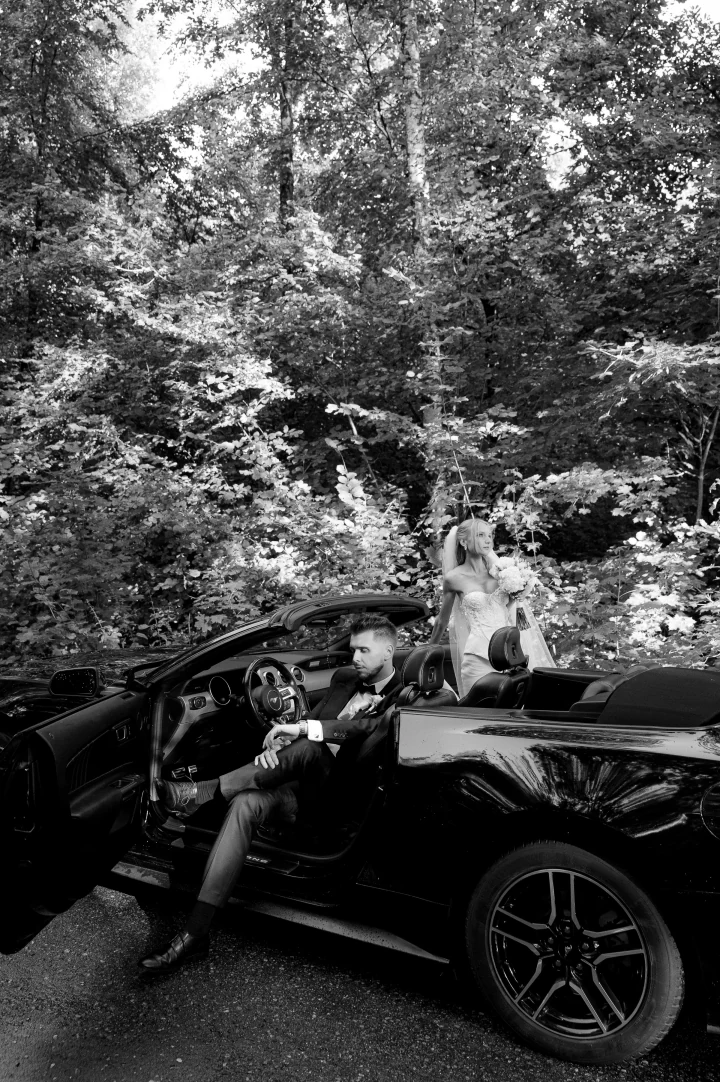 Pan Młody przy kierownicy cabrio i Panna Młoda obok, fotografia czarno-biała