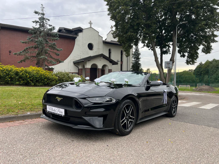 Mustang z kwiatami na masce i białymi wstążkami przed kościołem