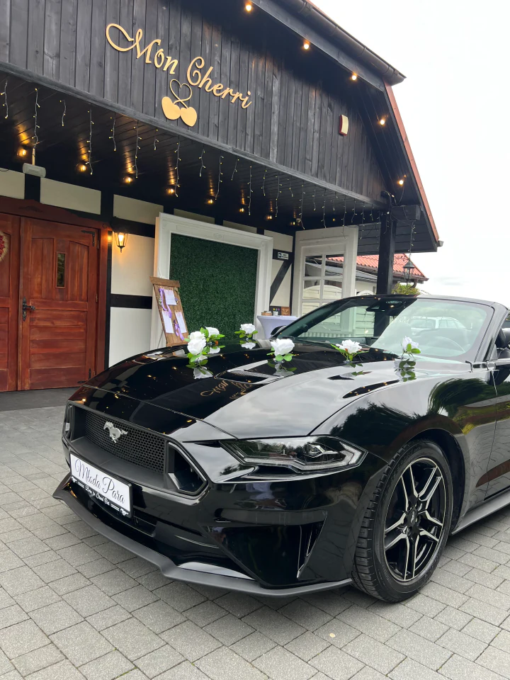 Mustang Cabrio z białymi kwiatami na masce przed salą weselną Mon Cherri