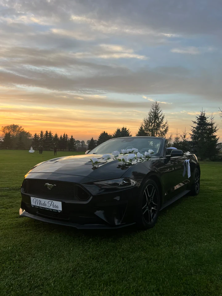 Mustang z białymi różami na masce podczas sesji ślubnej o zachodzie słońca