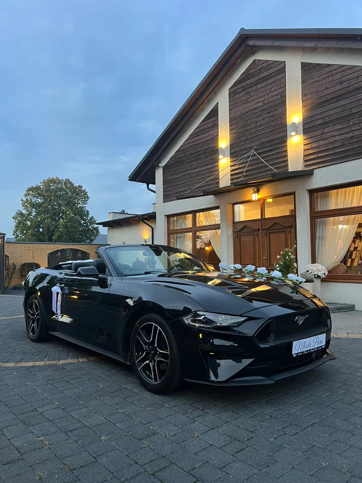 Udekorowany Mustang Cabrio przed oświetloną salą weselną