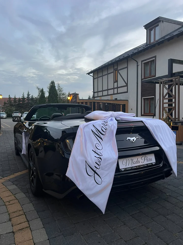 Biała kokarda Just Married i tablica Młoda Para na tyle Mustanga przed salą weselną